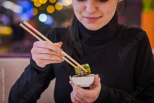 Eating sushi in the restaurant, a woman with a perfect manicure using chopsticks takes a piece of roll, enjoying tasty and healthy food, traditional Asian dish close up