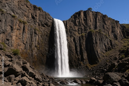 A towering waterfall shot from below in a lush region with a bright sky backdrop
