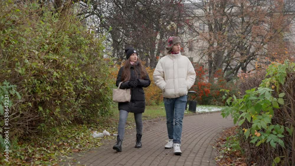 A young woman leads a conversation, guiding her male friend through an urban park. They walk on a cold day with the first snow on the ground, exploring the city and enjoying their time together. A young woman leads a conversation, guiding her male friend through an urban park. They walk on a cold day with the first snow on the ground, exploring the city and enjoying their time together.