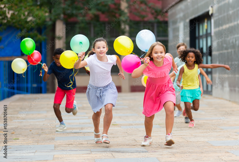 Obraz premium Portrait of cheerful preteen girls and boys with colorful toy balloons in hands running on city street on sunny summer day