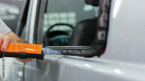 Worker applies special adhesive sealant to windscreen before installation on auto.