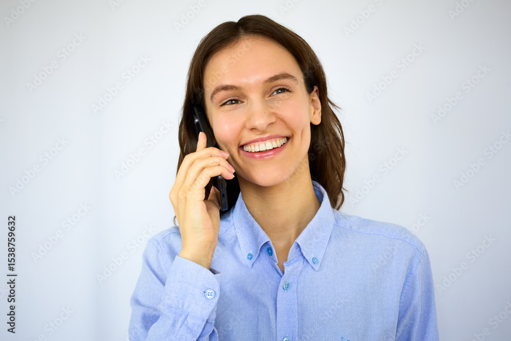 Beautiful happy brunette with the big smile in a blue shirt talking on her mobile phone on the white background Beautiful happy brunette with the big smile in a blue shirt talking on her mobile phone on the white background