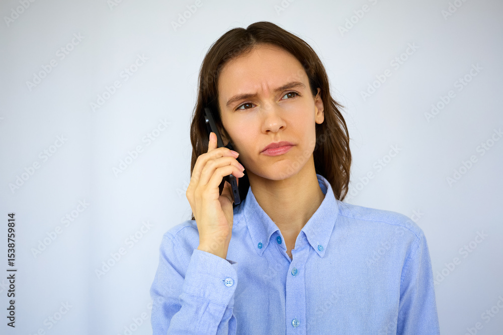 Beautiful angry brunette in a blue shirt talking on her mobile phone on the white background Beautiful angry brunette in a blue shirt talking on her mobile phone on the white background