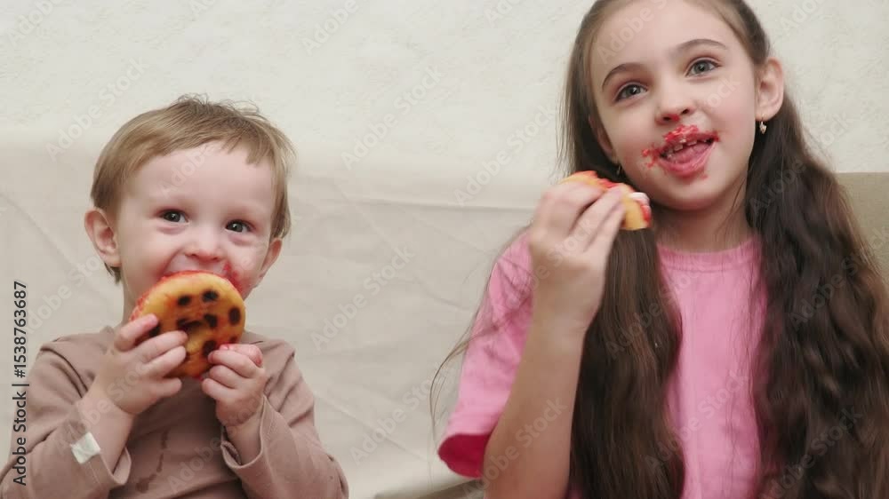 Cute little boy with blond hair and girl, brother and sister having fun with glazed donuts sticking his tongue out. Children and sweet junk food concept. Kid eating sweets at home Cute little boy with blond hair and girl, brother and sister having fun with glazed donuts sticking his tongue out. Children and sweet junk food concept. Kid eating sweets at home