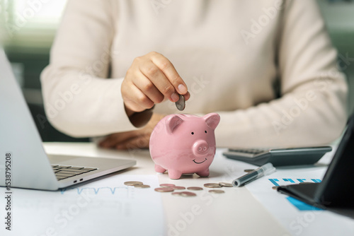 Fototapeta Naklejka Na Ścianę i Meble -  Female hand holding a pink piggy bank with coins in it. Investment concept of saving money. Saving money, planning and accounting.