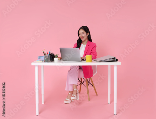 Beautiful asian businesswoman working white computer laptop sitting at the table office isolated on pink background.
