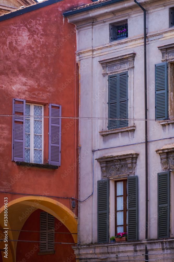 Naklejka premium Reggio Emilia, Italy, 01.04.2025.Old European building facades with red wall, grey shutters and arches, urban detail