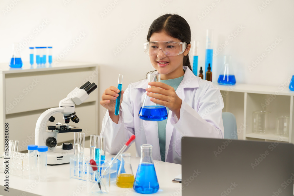 Fototapeta premium Asian schoolgirl wearing lab coat and goggles smiles while holding beaker and test tube in science classroom, reflecting joy and excitement in hands-on laboratory learning experience.
