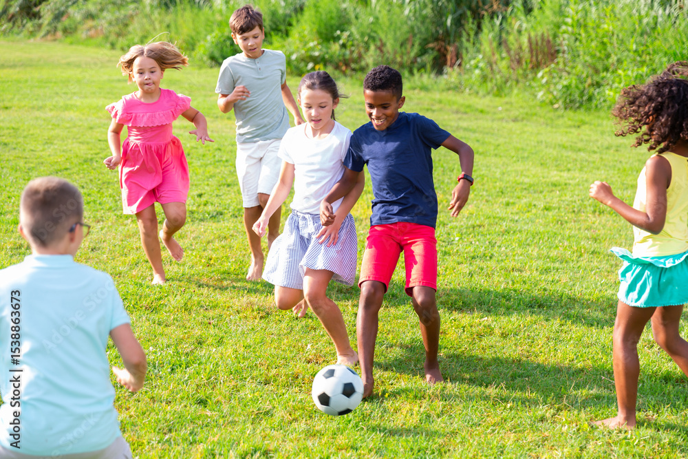 Obraz premium Positive kids running on field and playing football together.