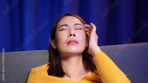 Video 4k of Asian woman is resting on the sofa looking unwell with a headache and fever. She appears stressed tired and exhausted from cold flu or illness at home
