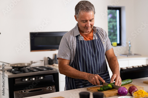Senior man slicing cucumber into thin rounds at kitchen island with wooden cutting board