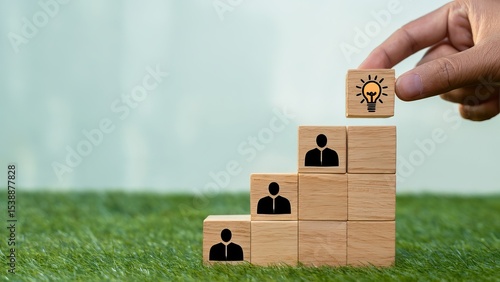 Hand placing lightbulb block on top of leadership cubes illustrating business and career success, ideas and innovation on green background