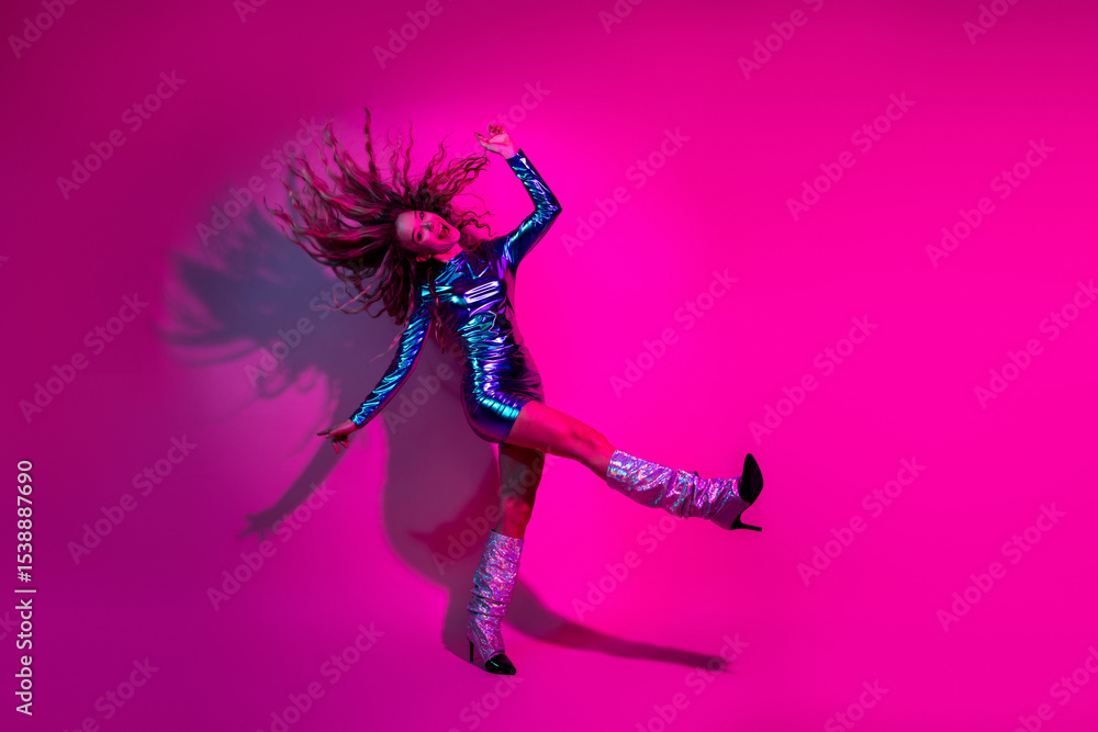 Young woman in a shiny blue dress joyfully dancing against a vibrant pink background, capturing a lively and glamorous fashion Young woman in a shiny blue dress joyfully dancing against a vibrant pink background, capturing a lively and glamorous fashion