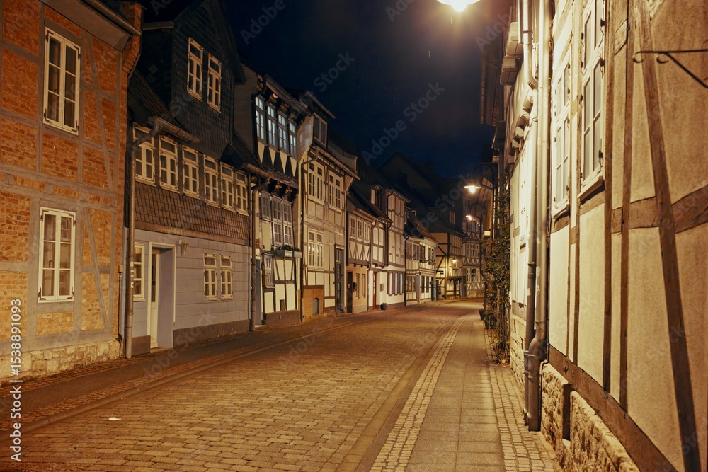 Naklejka premium Quiet medieval street lined with timber-framed houses illuminated by warm night lighting in a historic German town.