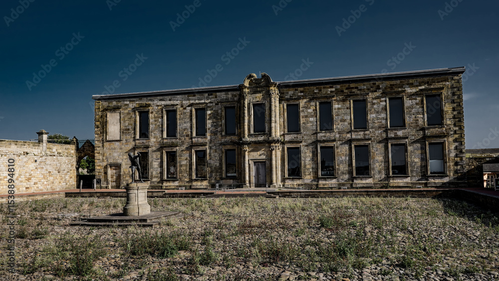 Fototapeta premium Whitby Abbey house facade with statue in the foreground, located in Whitby, North York Moors National Park, UK, on a sunny day with blue sky
