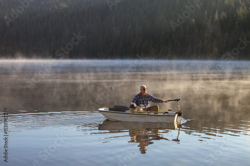 Elderly man and his dog cruising in a small fiberglass fishing boat with an electric motor on Elk River Reservoir in Idaho