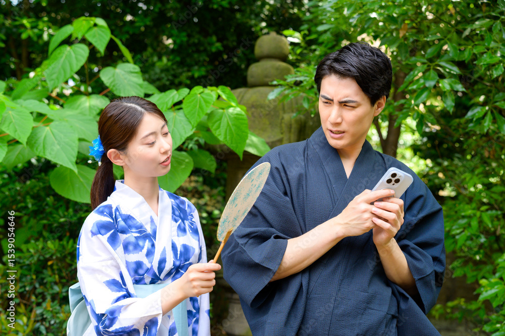 Obraz premium 浴衣姿の女性がスマートフォンを操作する男性をのぞき込もうとするも男性が不快感を示す夏の一場面