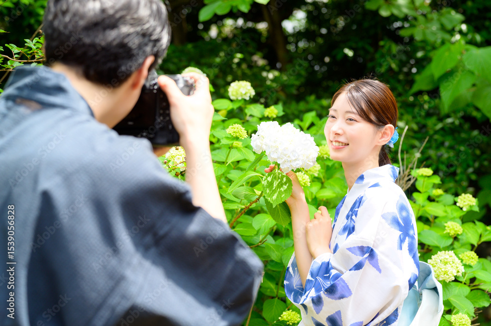 Obraz premium 浴衣の女性が紫陽花のそばで笑顔を見せる姿をカメラで撮影する和やかな夏の撮影風景