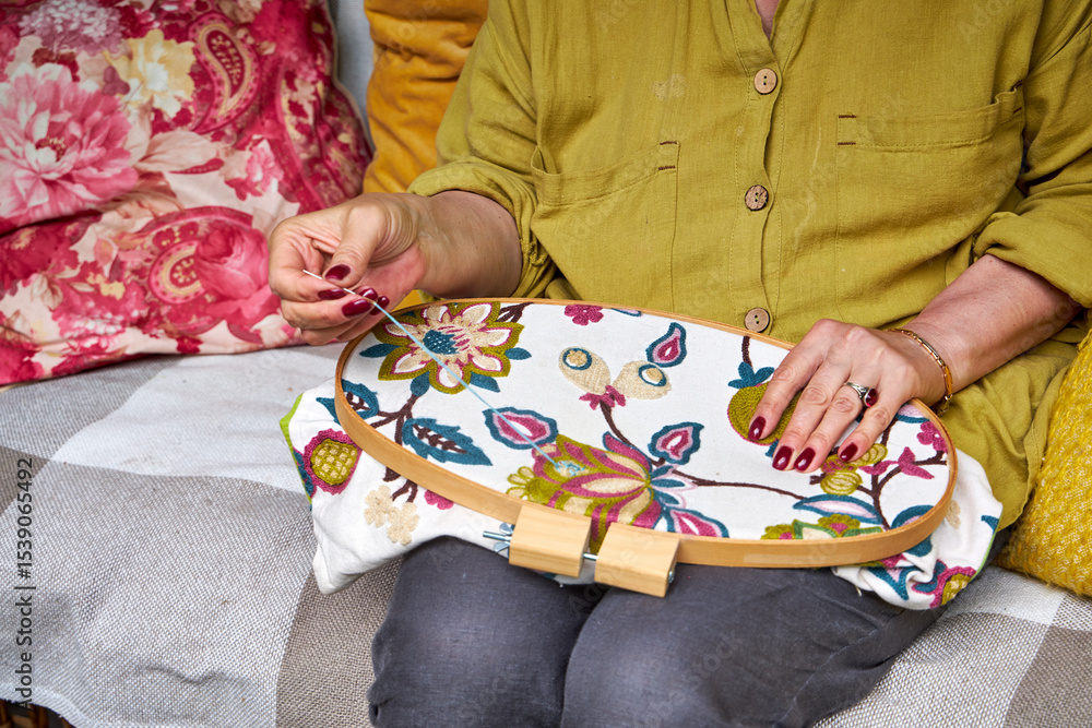 Obraz premium Front close-up view of a woman's hands embroidering a decorative pattern on fabric stretched in an embroidery hoop. The hands are focused and steady, with visible stitches forming on the fabric. Natur