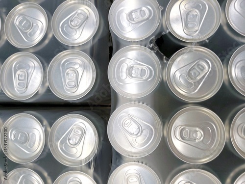 Top view of aluminum drink cans tightly packed in shrink wrap. repetitive pattern of can tops, beverage industry, mass production, and recycling