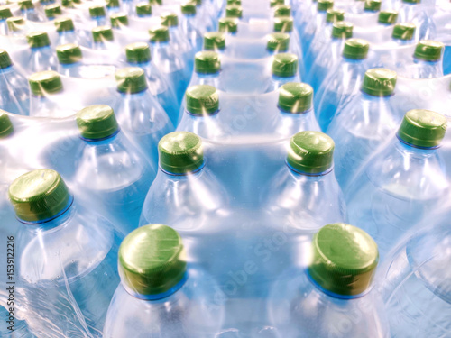 Multiple plastic water bottles tightly packed in shrink wrap, seen from above. Green caps, blue-toned bottles, clean, fresh visual, hydration, mass production, bottled water industry, packaging