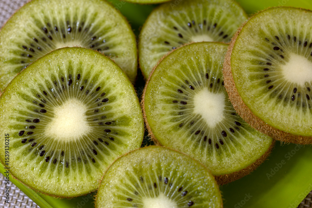 Sliced kiwi fruit arranged on a green plate. The vibrant green flesh and small black seeds are clearly visible, showcasing the fruit's unique texture and color. Sliced kiwi fruit arranged on a green plate. The vibrant green flesh and small black seeds are clearly visible, showcasing the fruit's unique texture and color.