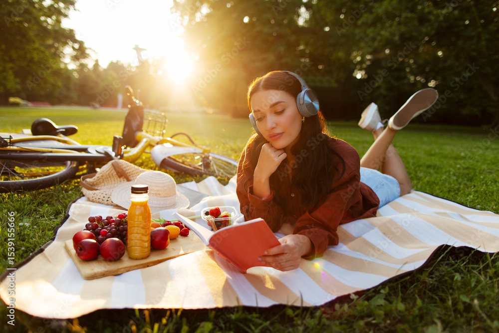 Ταπετσαρία Carefree woman listening to music in headphones, lying on picnic mat and reading