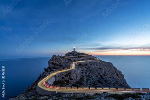 Blue hour image of light trails on winding hairpin road, leading to the Far the Formentor lighthouse, positioned on dramatic cliff landscape next to the ocean on Mallorca, Spain