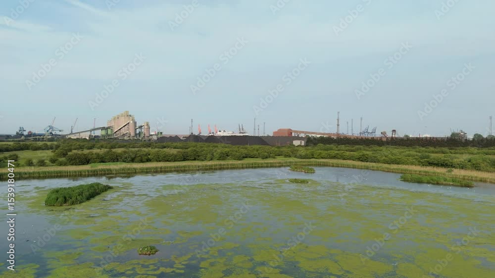 Aerial drone shot of wetland with birds flying contrasting with large industrial coal iron ore raw materials storage and loading reclaimer dumper truck heavy machinery Immingham port harbour England Aerial drone shot of wetland with birds flying contrasting with large industrial coal iron ore raw materials storage and loading reclaimer dumper truck heavy machinery Immingham port harbour England