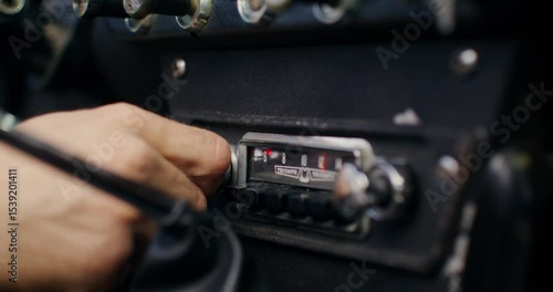 The man turns on the radio in the car, close-up of his hand as he turns the screw