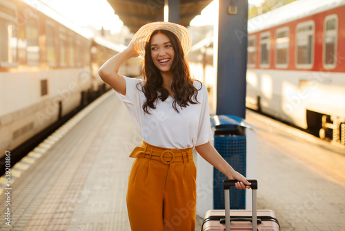 European lady waiting her train at the railway station, walking with suitcase, starting her summer trip. Public rail transportation