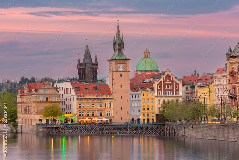 Colorful buildings and towers along the Vltava River in Prague Czech Republic at sunset with calm water and vibrant sky Colorful buildings and towers along the Vltava River in Prague Czech Republic at sunset with calm water and vibrant sky