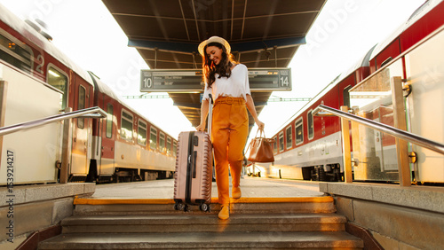 Happy woman tourist with suitcase getting down the stairs of railway station platform, arriving to new city for vacation