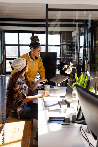 Collaborating on coding project, diverse women focused in modern office
