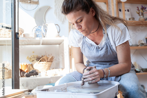 Focused ceramic artist shaping clay on wheel in her workshop