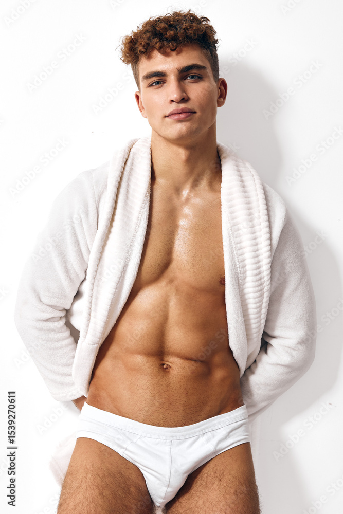 Fototapeta premium Confident young man posing in white underwear with towel wrapped around his shoulders, showcasing an athletic build. Concept of fitness and self-assurance.