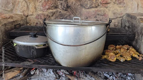 Traditional Colombian sancocho cooking over firewood on a rustic grill, alongside chicken pieces and another pot with delicious homemade food, rich in flavor, cultural cuisine outdoor kitchen setting