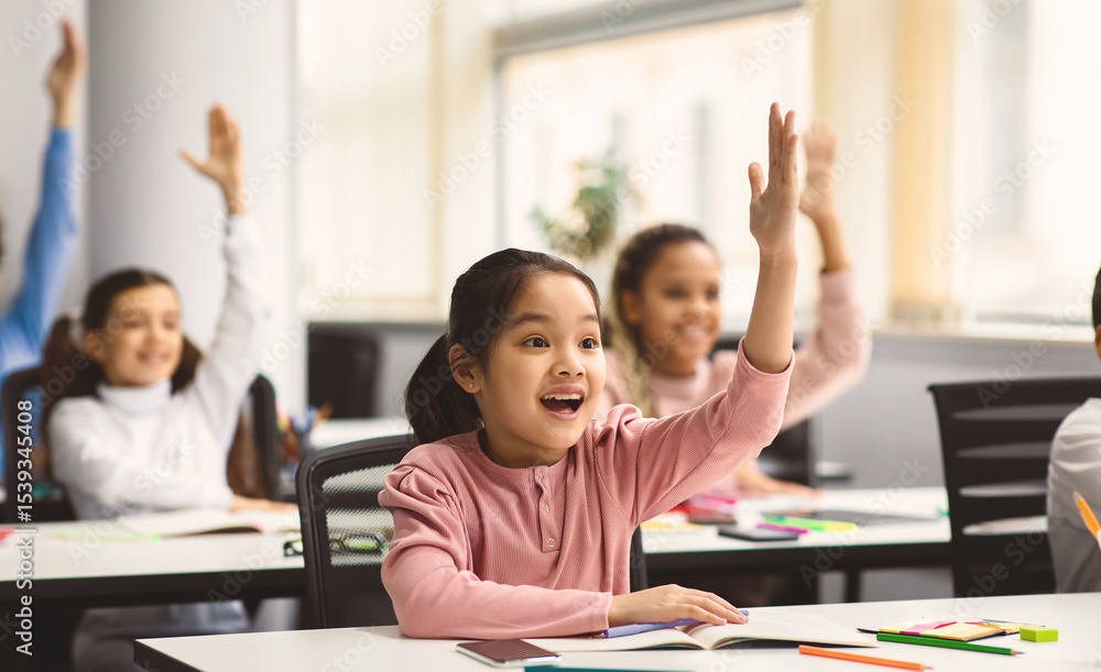 Education, Elementary School, Learning and People Concept. Diverse group of smart junior school kids sitting at desks in classroom and raising hands for an answer, studying with pleasure Education, Elementary School, Learning and People Concept. Diverse group of smart junior school kids sitting at desks in classroom and raising hands for an answer, studying with pleasure