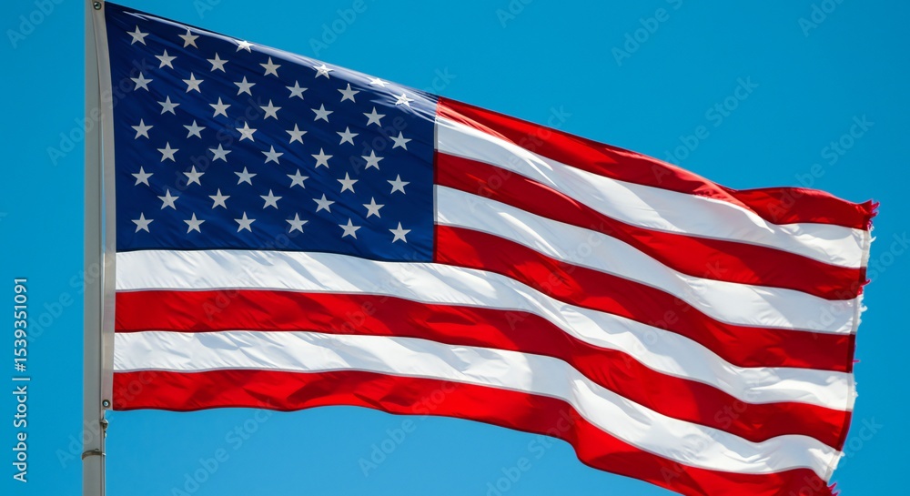 Fototapeta premium A flowing American flag against a bright blue sky, showcasing vivid red and white stripes with a blue canton filled with stars, highlighting patriotism.