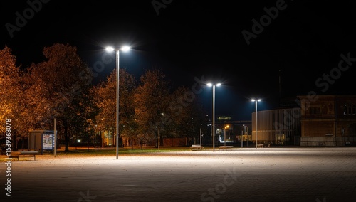 Empty city square at night, illuminated by streetlights.  Trees with autumn foliage