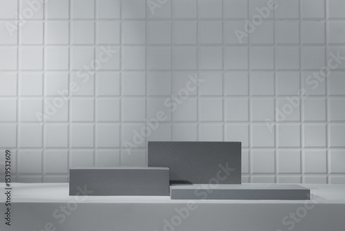 Dark grey rectangular podiums arranged symmetrically on grey tile base. Set against pale white-tiled wall  the composition provides contrast for bold product display.