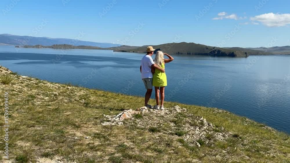 A couple relaxes by the stunning waters of Lake Baikal, capturing joyful memories under the summer sun. A couple relaxes by the stunning waters of Lake Baikal, capturing joyful memories under the summer sun.