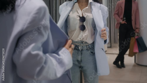 Close-up of a young woman trying on a jacket in a changing room, checking herself in the mirror while her boyfriend observes from behind.