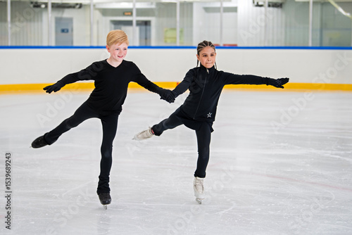 Two young figure skaters skate on the ice of an indoor skating rink.