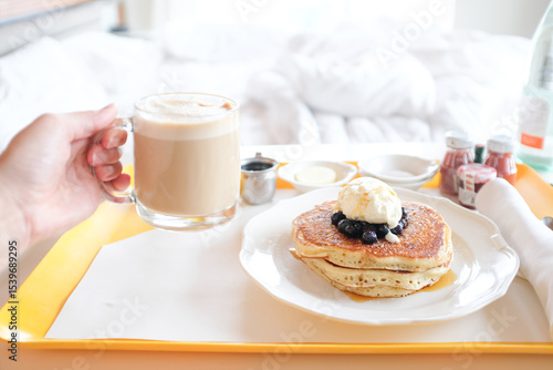 Фотография Room Service tray with pancakes and cappuccino with bed in background
