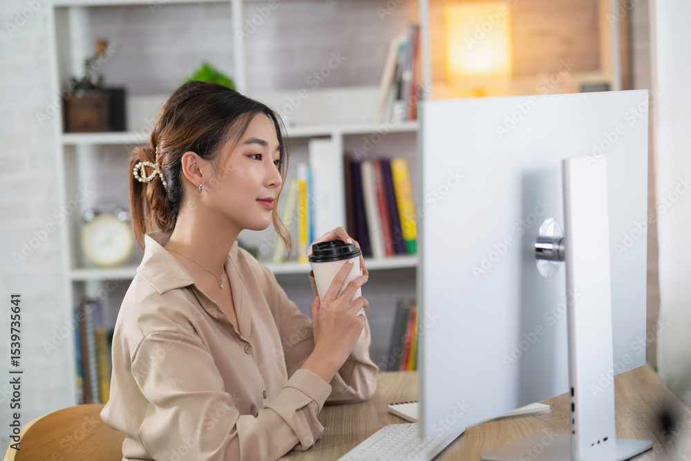 Young Woman Enjoys Coffee While Working at Modern Home Office Desk with Computer and Bookshelf in Cozy Bright Environment Young Woman Enjoys Coffee While Working at Modern Home Office Desk with Computer and Bookshelf in Cozy Bright Environment
