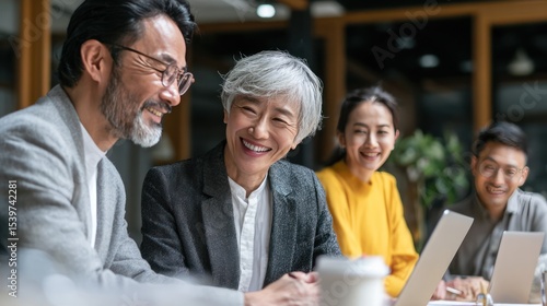 Candid teamwork moment with mature Asian business leader teaching junior team members, modern office setting with digital tools, professional and friendly tone