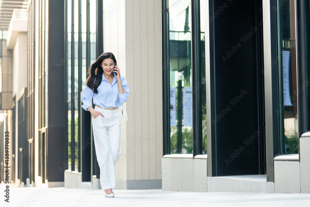 Fototapeta premium Asian young businesswoman talking on smartphone while walking in city.