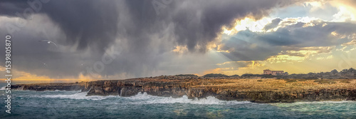 Dramatic Stormy Sky Over Mediterranean Rocky Coastline with Sunbeams and Waves