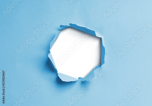 Close-up image of a blue paper sheet with a jagged hole torn through the center, revealing a transparent background.